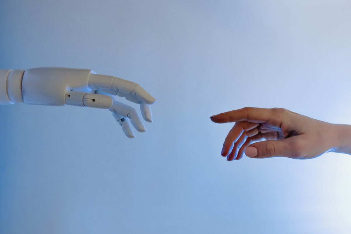One robot hand and one human hand reaching out to point figures